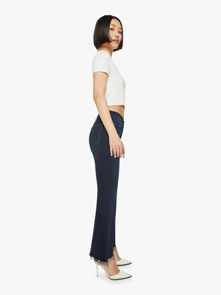 Side view of a dark blue mid-rise flare has a 29-inch inseam with a frayed hem.