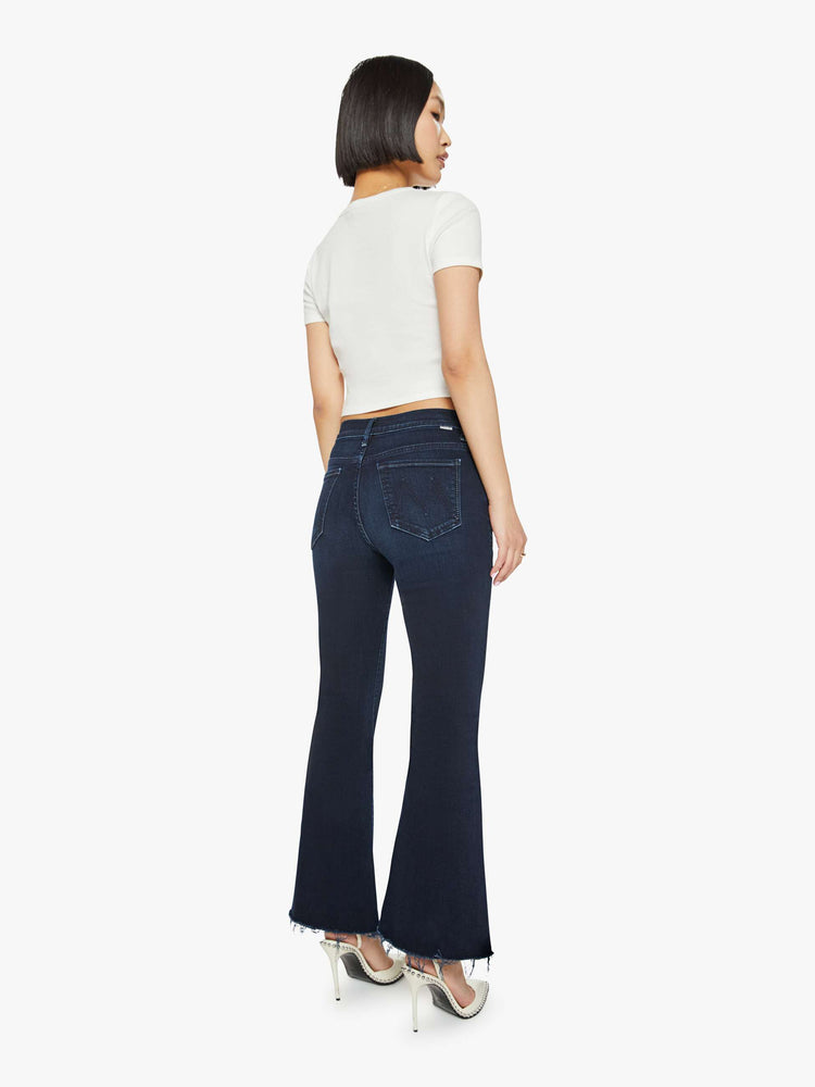 Back view of a dark blue mid-rise flare has a 29-inch inseam with a frayed hem.