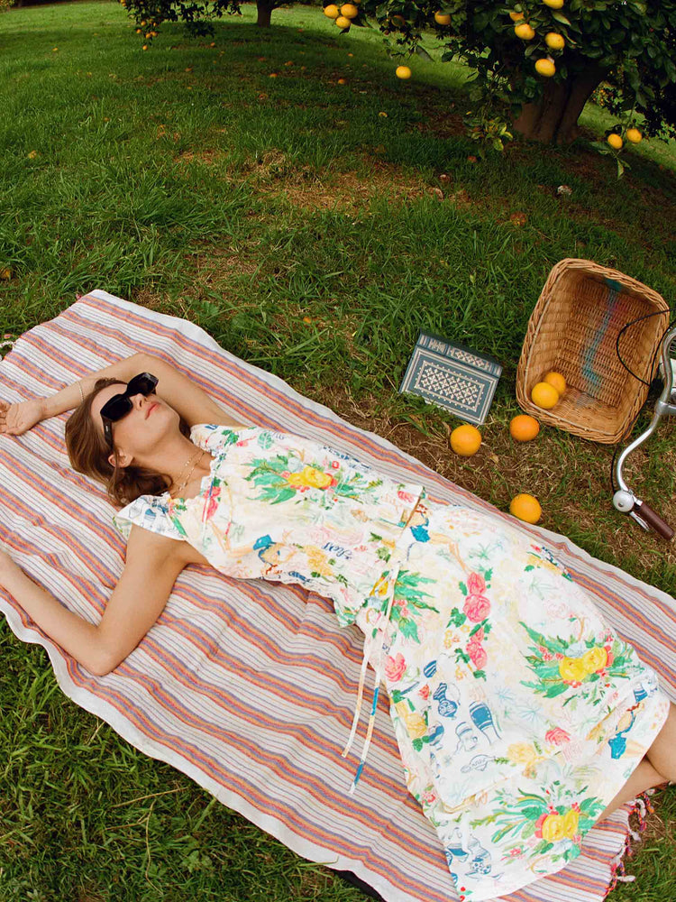 Editorial image of a woman lying on a towel in a garden, wearing a printed top and skirt set.