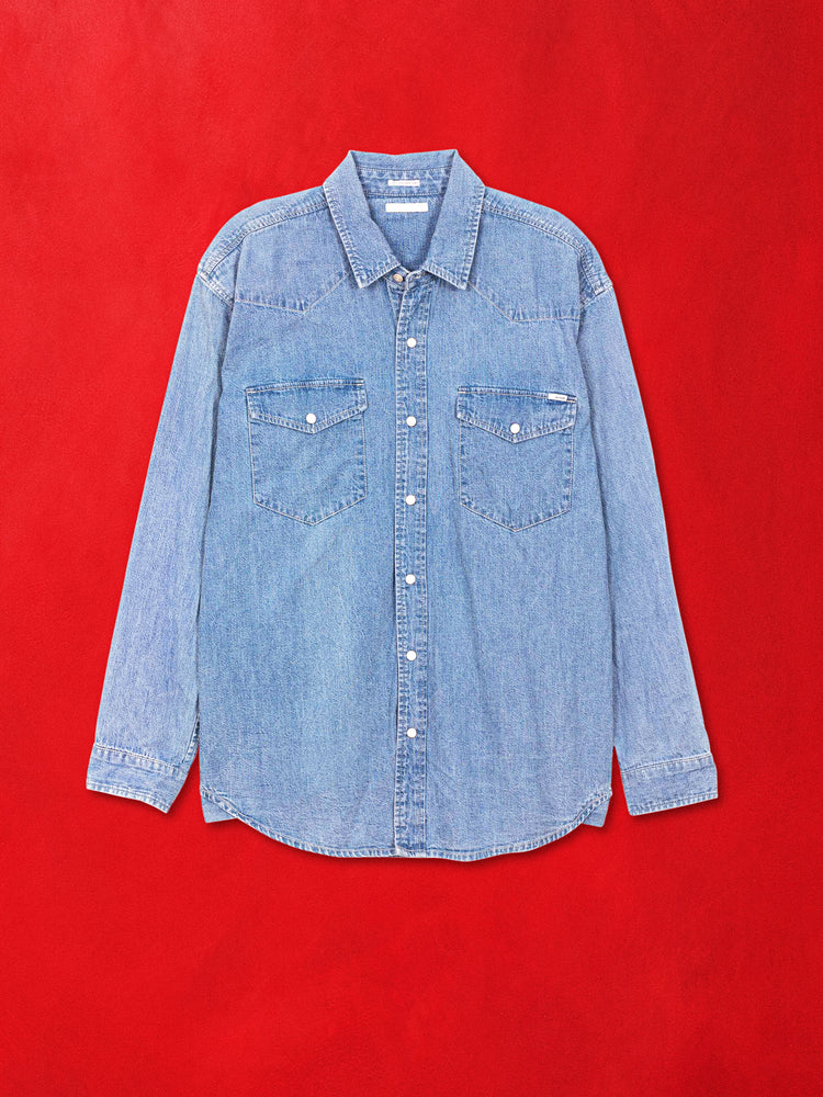 A flat product image of blue denim shirt against a red background.