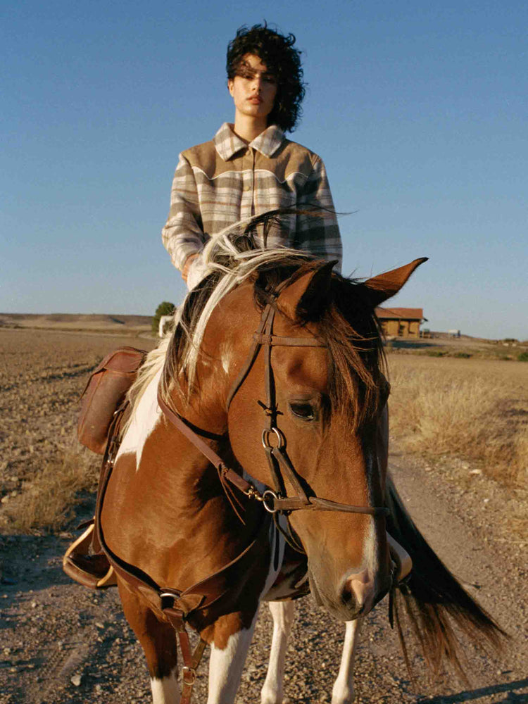 Editorial shot of  view of a tan plaid collared jacket with a Western-inspired yoke and snaps down the front. 