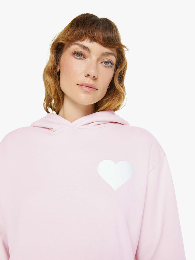 Close up view of a woman in a pink with white heart sweatshirt with a front patch pocket and a loose, comfortable fit.