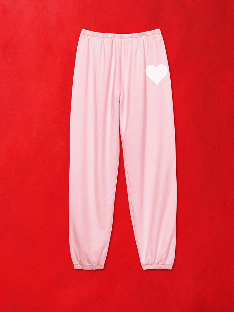 A flat image of light pink sweatpants with a white heart, against a red background.