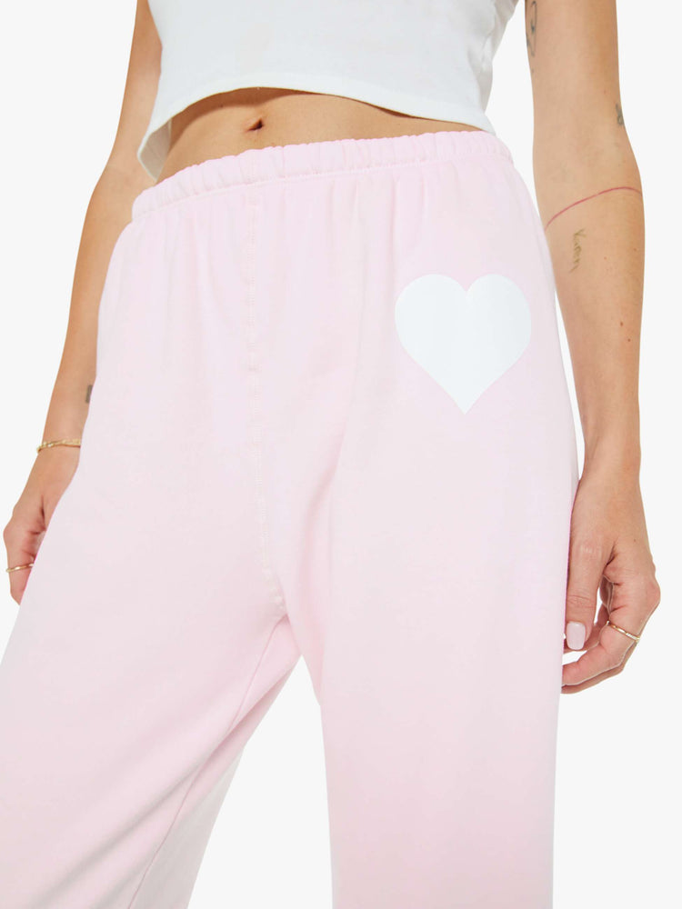 Close up view of a woman's pink sweatpant with a white heart on the hip and an elastic waist and cuffs for a loose, comfortable fit.