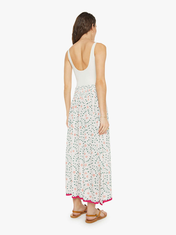 Back  view of a woman in a off-white with a colorful floral print, and features a smocked waistband and a loose, flowy fit maxi skirt.