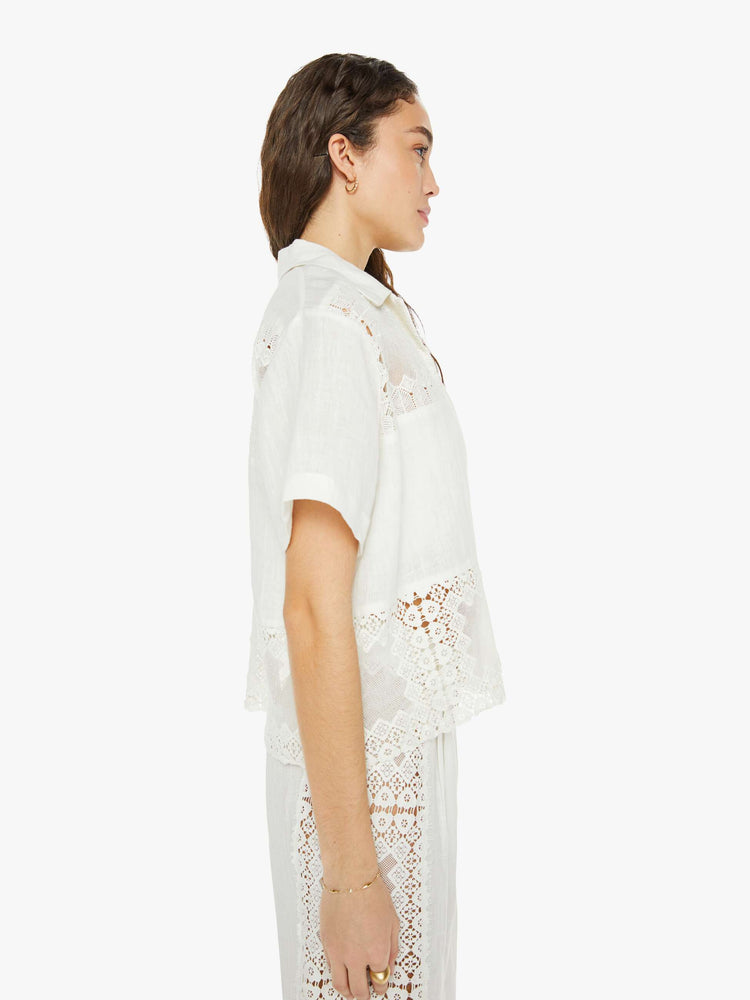 Side view of a woman short sleeve button up in off-white, and features a buttoned V-neck, slightly dropped shoulders and a boxy fit.