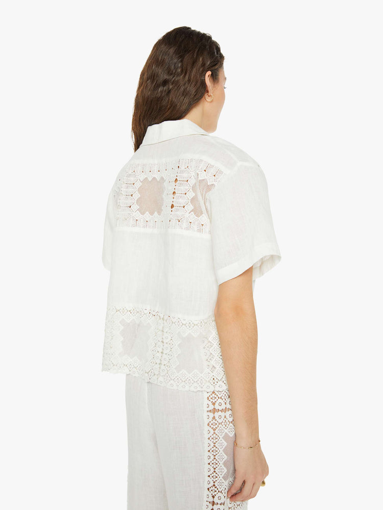 Back view of a woman short sleeve button up in off-white, and features a buttoned V-neck, slightly dropped shoulders and a boxy fit.