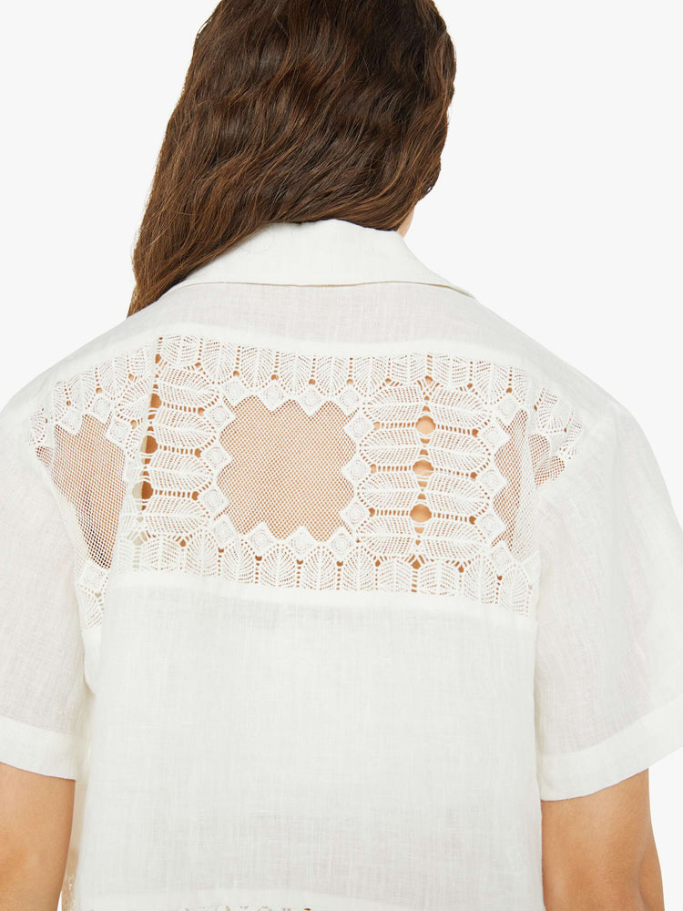 Back view of a woman short sleeve button up in off-white, and features a buttoned V-neck, slightly dropped shoulders and a boxy fit.