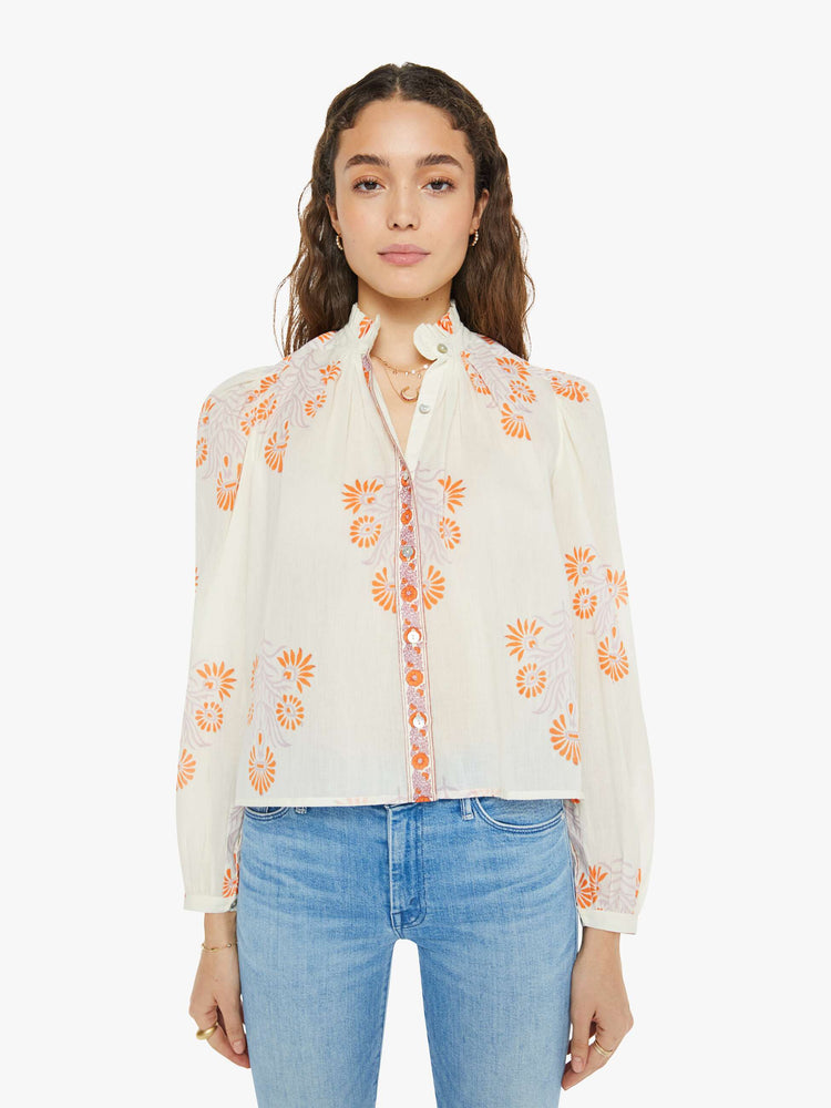 Front view of a woman long sleeve blouse in white with a warm-toned tropical print, and features ruffled collar, puffed shoulders, long balloon sleeves, buttons down the front and a slightly cropped fit.