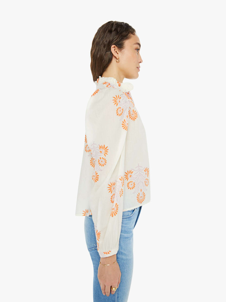 Side view of a woman long sleeve blouse in white with a warm-toned tropical print, and features ruffled collar, puffed shoulders, long balloon sleeves, buttons down the front and a slightly cropped fit.