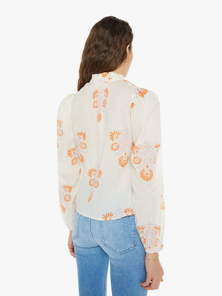 Back view of a woman long sleeve blouse in white with a warm-toned tropical print, and features ruffled collar, puffed shoulders, long balloon sleeves, buttons down the front and a slightly cropped fit.