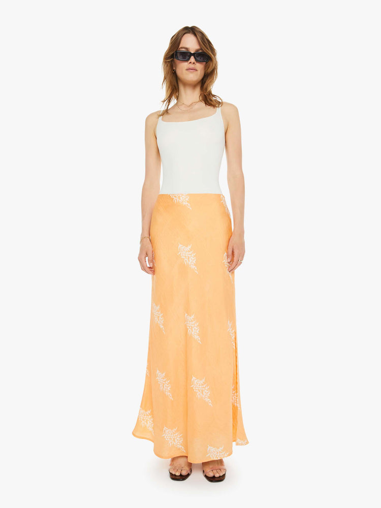 Front view of a silk skirt in a peachy-orange with a light pink floral print, and features a slightly narrow A-line fit.