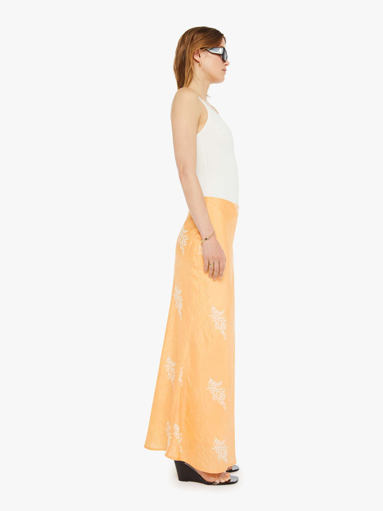 Side view of a silk skirt in a peachy-orange with a light pink floral print, and features a slightly narrow A-line fit.