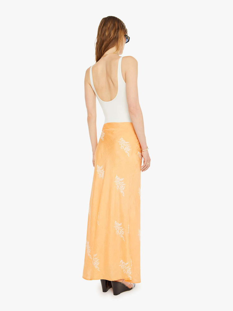 Back view of a silk skirt in a peachy-orange with a light pink floral print, and features a slightly narrow A-line fit.