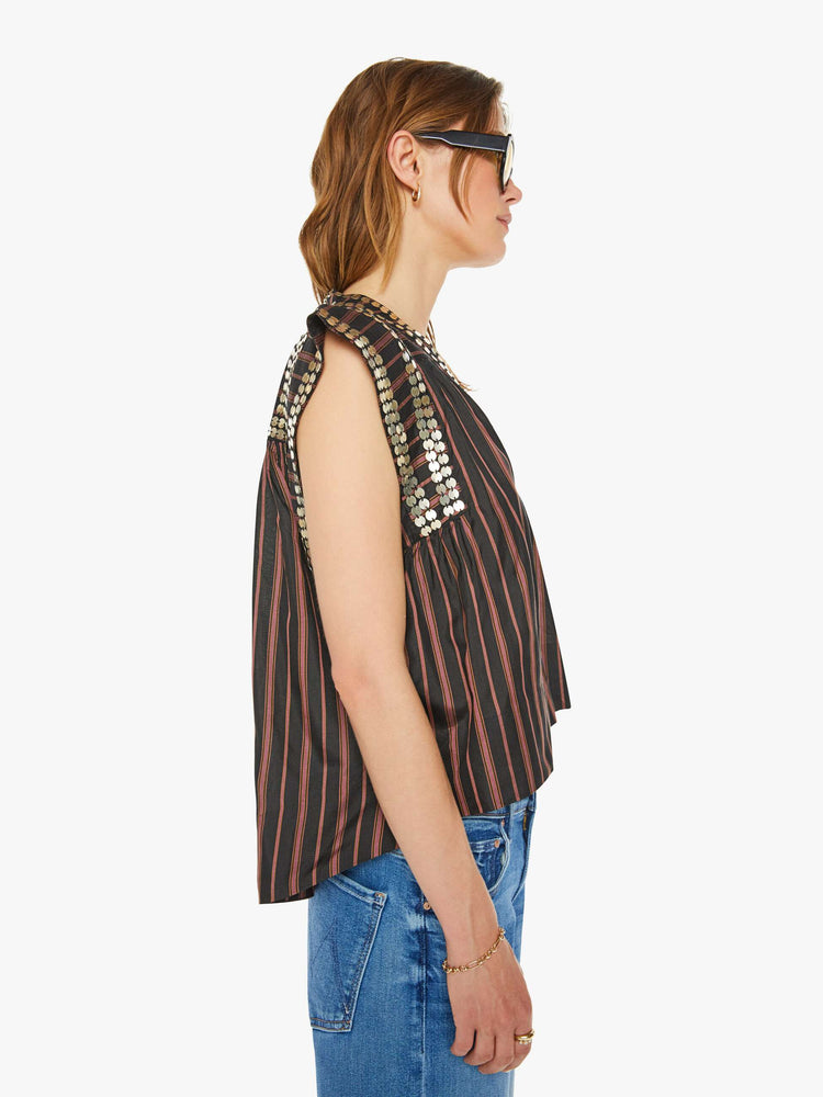 Side view of a woman brown with vertical black stripes in a scoop neck, structured short sleeves, a loose fit and coin embellishments throughout.