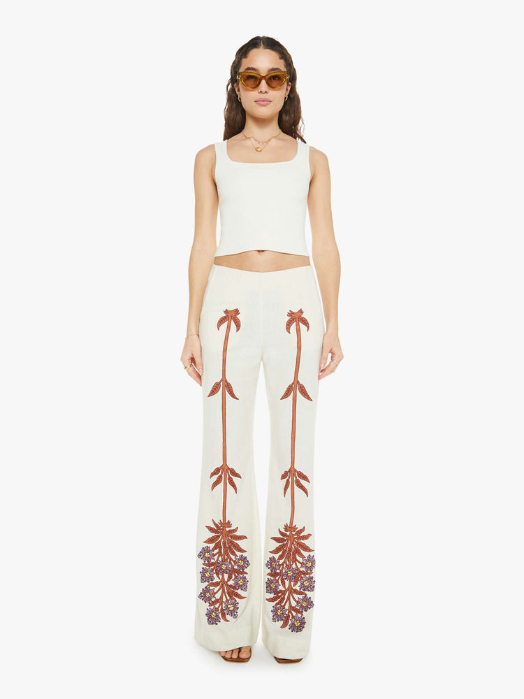 Front view of a woman  high rise, slit pockets, a loose flared leg and slightly cropped hem in off-white with a floral design in maroon down the front of the legs.