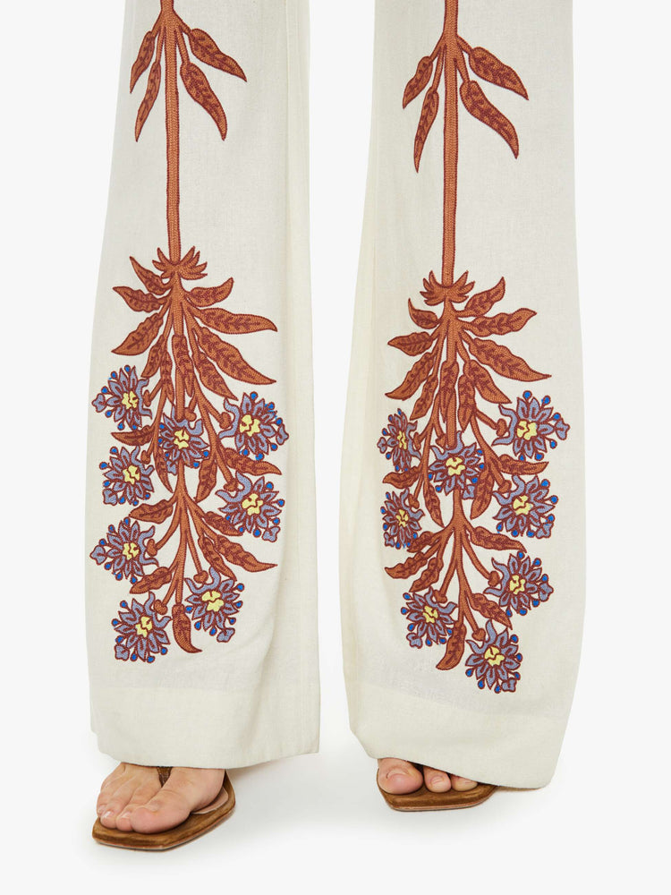 Front swatch view of a woman high rise, slit pockets, a loose flared leg and slightly cropped hem in off-white with a floral design in maroon down the front of the legs.