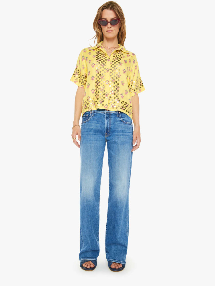 Full body  view of a woman short sleeve button-up in pastel yellow with a delicate floral print, and features a buttoned V-neck, slightly dropped shoulders, a boxy fit and coin embellishments throughout.