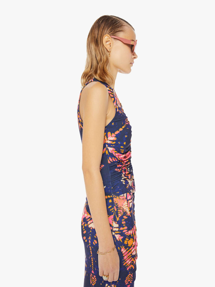 Side view of a woman in a deep navy with a warm-toned floral print, the sleeveless top features a high V-neck, a gathered seam down the front and a narrow fit.