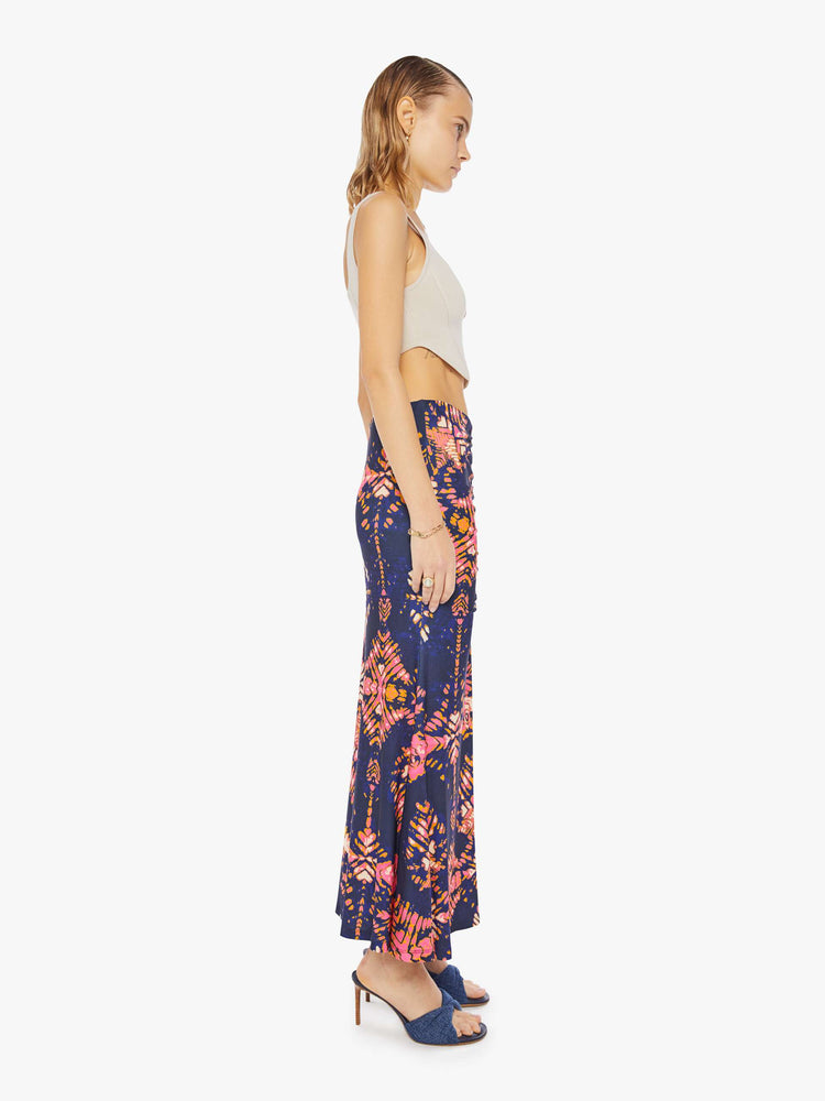 Side view of woman in a deep navy with a warm-toned floral print, the ankle-grazing skirt features a high rise, a gathered seam down the front and an A-line fit