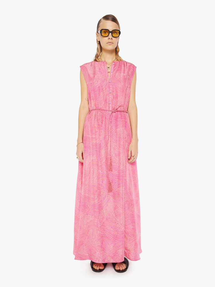 Front view of a woman  in pink with a delicate floral print, the sleeveless dress features a buttoned V-neck, a tied waist and a loose skirt with an ankle-grazing hem. 