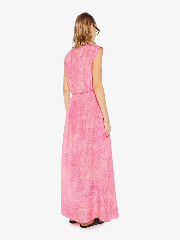 Back  view of a woman in pink with a delicate floral print, the sleeveless dress features a buttoned V-neck, a tied waist and a loose skirt with an ankle-grazing hem.