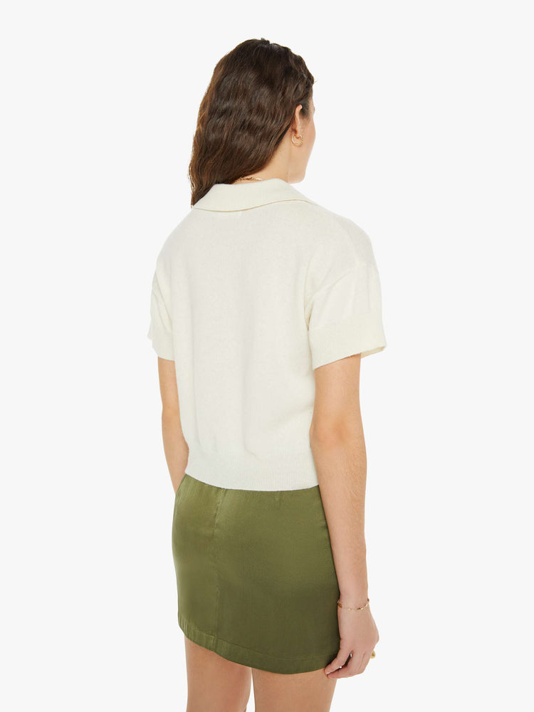 Back view of a woman in a knit polo with short sleeves, a V-neck and a slightly cropped fit.