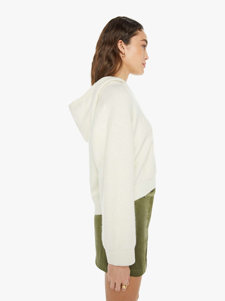 Side view of a woman in a creamy off white knit hoodie with a V-neck, front patch pocket and ribbed hems.