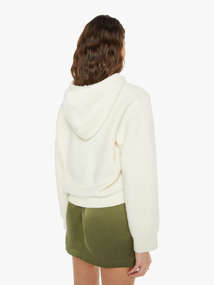 Back view of a woman in a creamy off white knit hoodie with a V-neck, front patch pocket and ribbed hems.