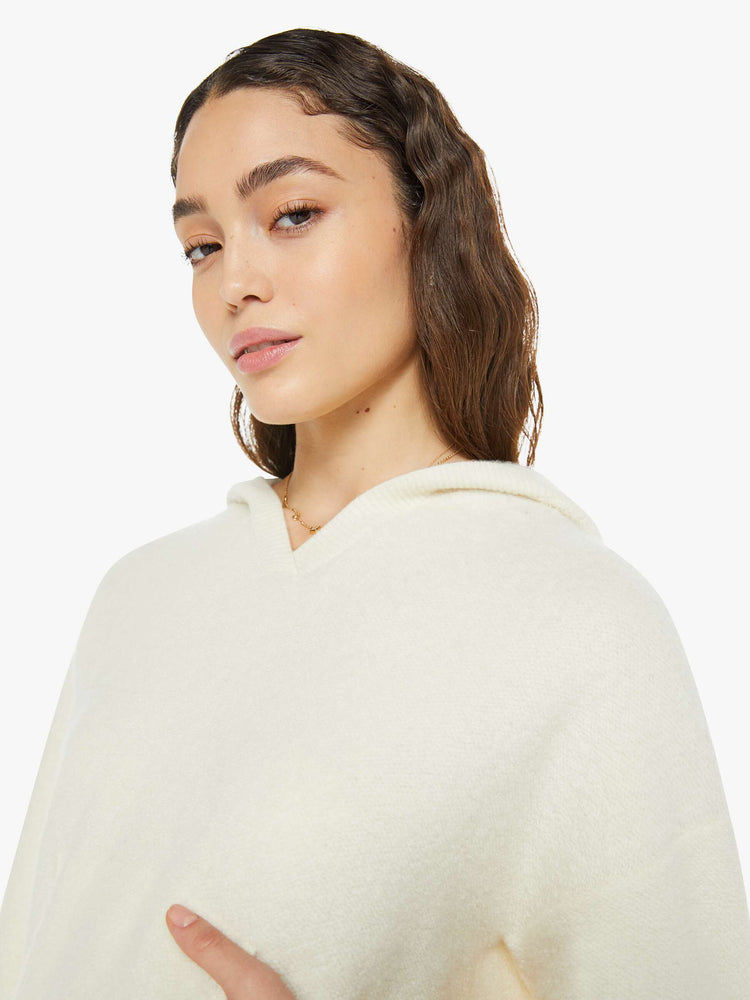 Close up view of a woman in a creamy off white knit hoodie with a V-neck, front patch pocket and ribbed hems.