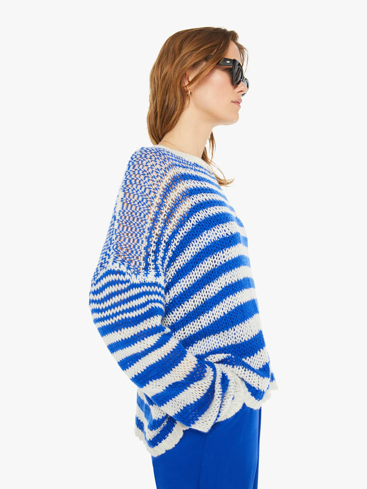 Side view of a woman in a blue and white striped knit crewneck with drop shoulders, long sleeves and an oversized fit.