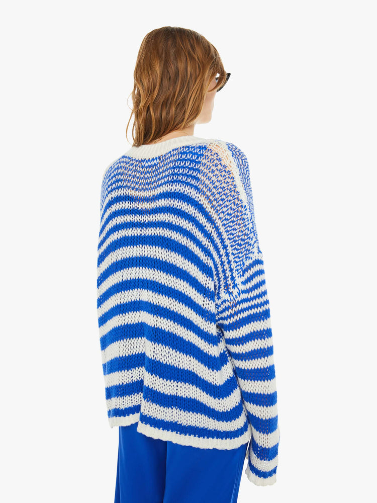 Back view of a woman in a blue and white striped knit crewneck with drop shoulders, long sleeves and an oversized fit.