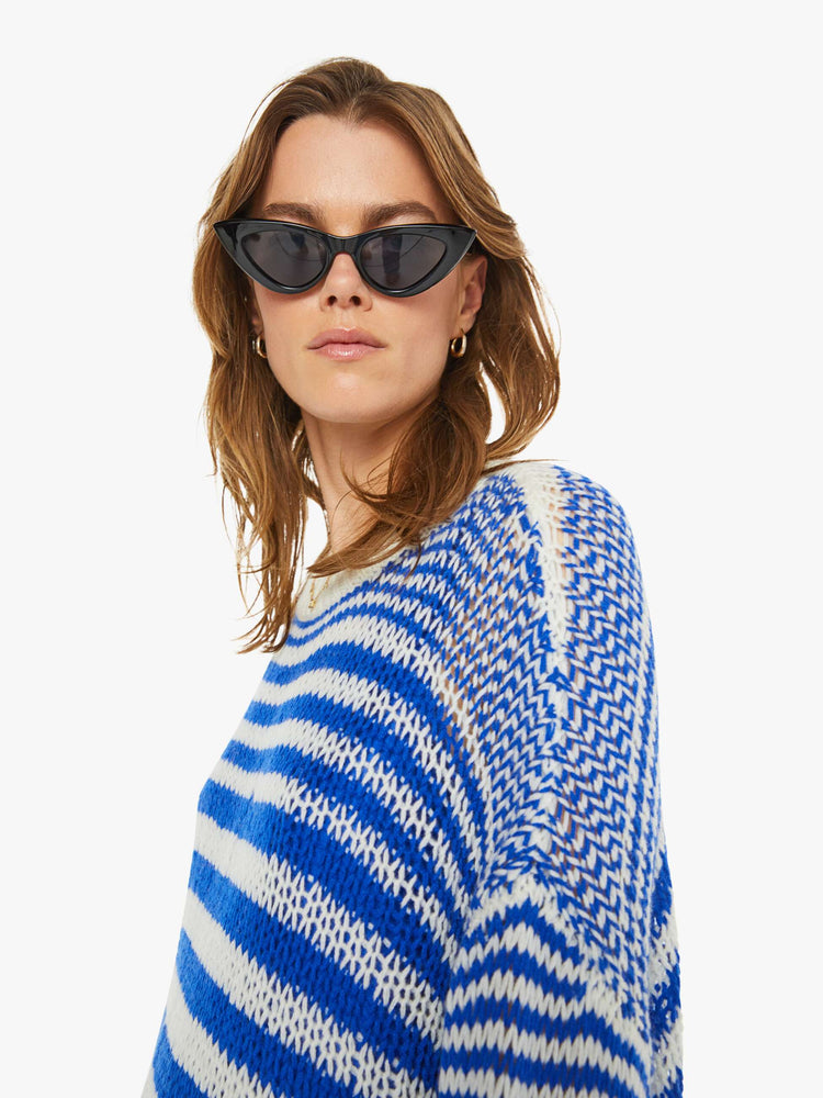 Detailed view of a woman in a blue and white striped knit crewneck with drop shoulders, long sleeves and an oversized fit.