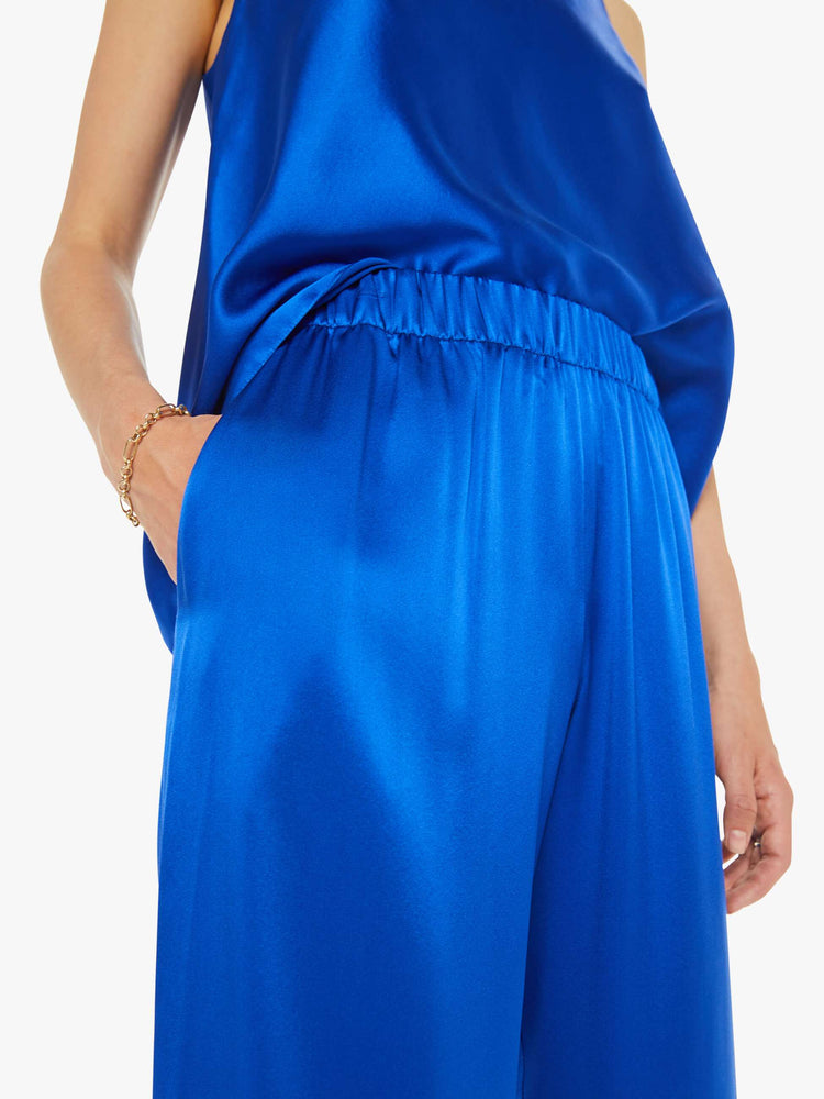 Close up view of a woman wide leg royal blue trousers with an elastic waist, side slit pockets and a loose, flowy fit.