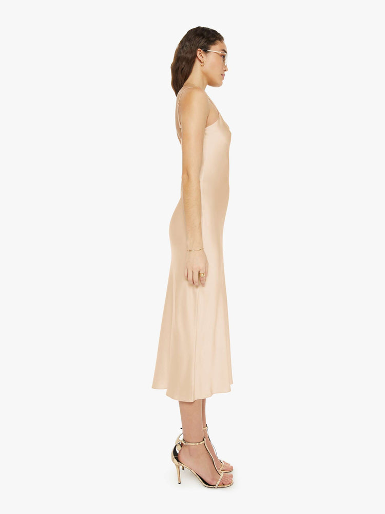 Side view of a woman in a light pink slip dress with a V-neck, thin spaghetti straps and a calf-length hem.