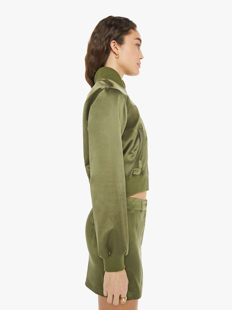 Side view of a woman in a green bomber jacker with a stacked collar, a zip closure, side slit pockets and a shrunken fit.