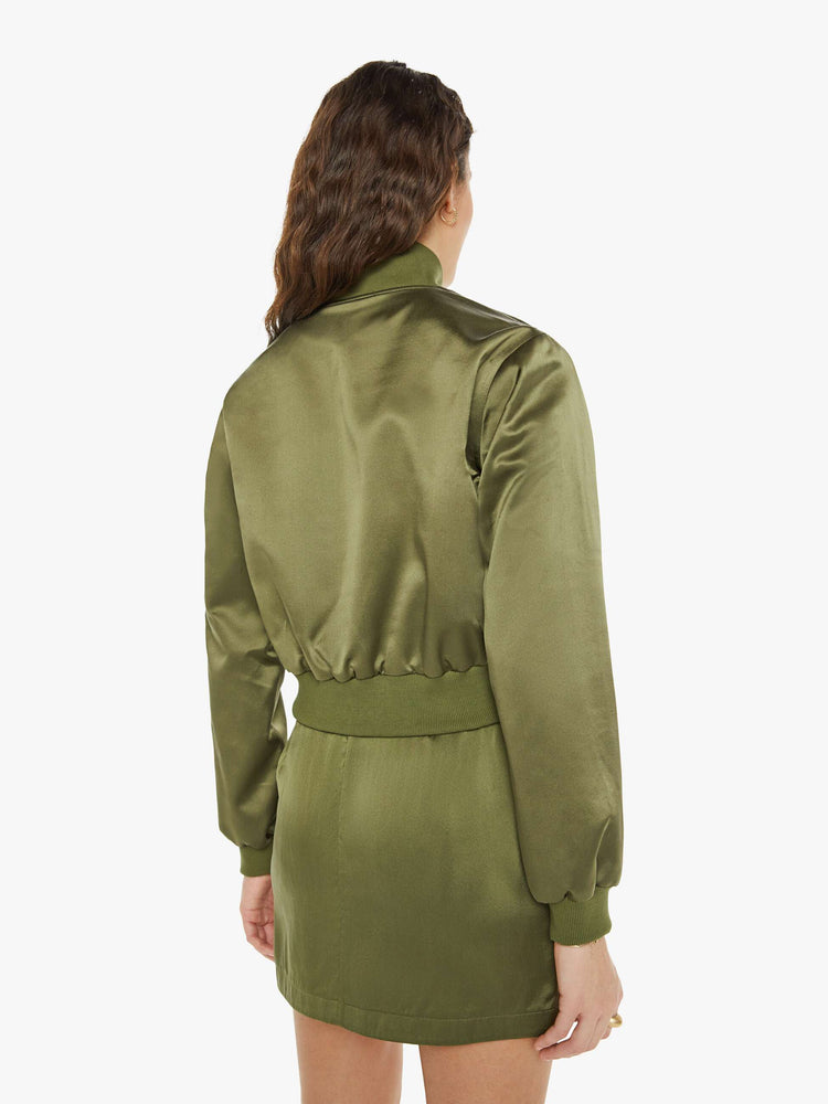 Back view of a woman in a green bomber jacker with a stacked collar, a zip closure, side slit pockets and a shrunken fit.