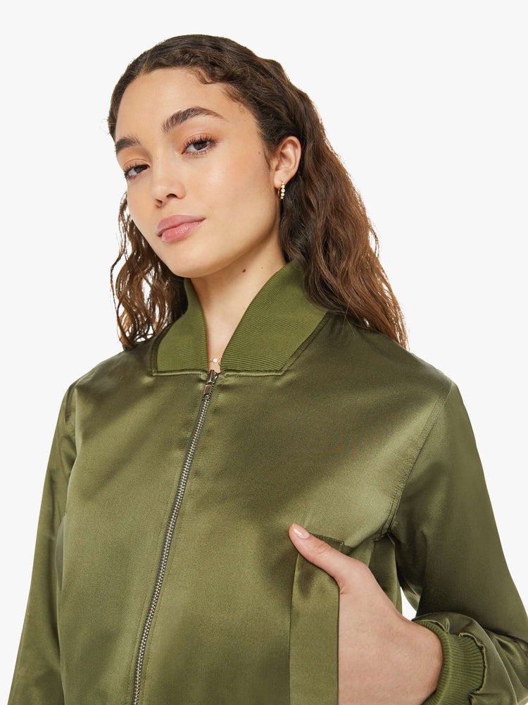 Close up view of a woman in a green bomber jacker with a stacked collar, a zip closure, side slit pockets and a shrunken fit.