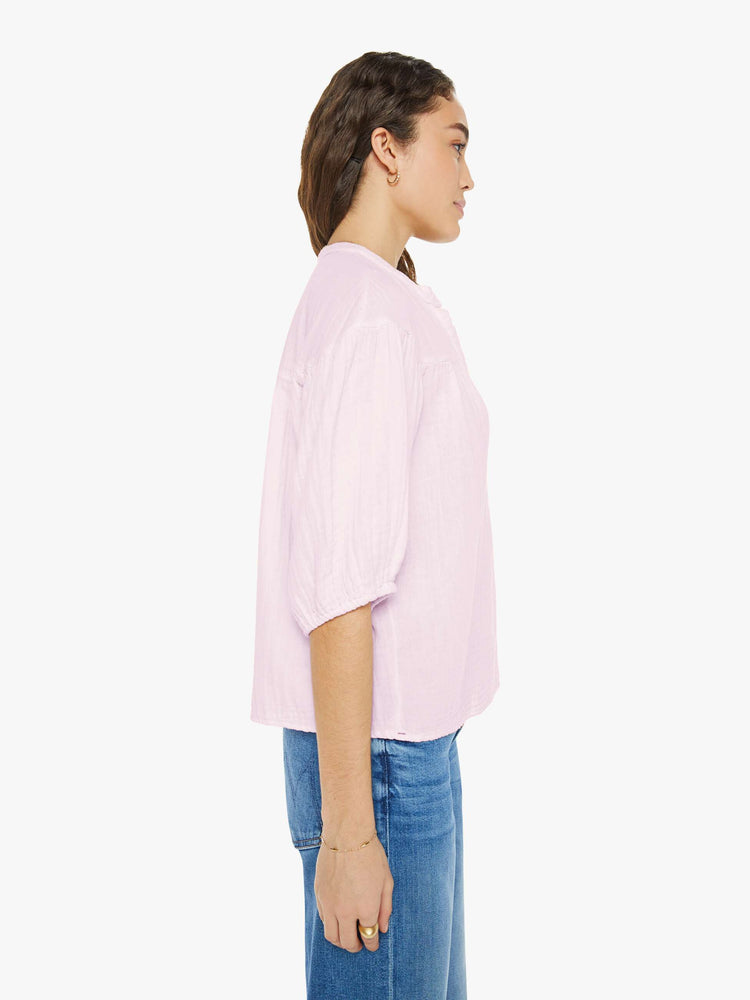 Side view of a woman in a light pink blouse that features a V-neck, elbow-length balloon sleeves and ruffles throughout for a loose, flowy fit.