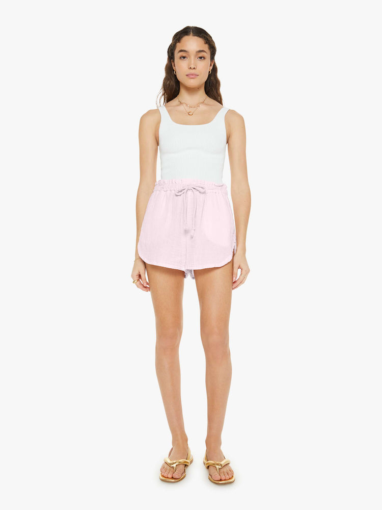 Front view of a woman in light pink shorts with a drawstring elastic waistband, curved hems and a loose, flowy fit.