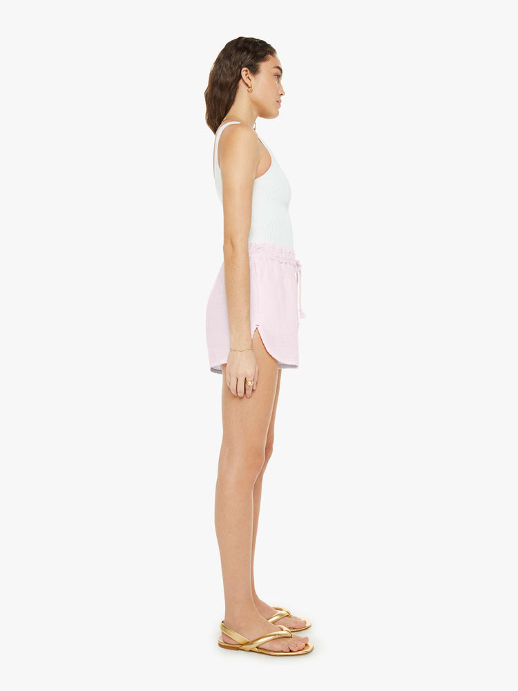 Side view of a woman in light pink shorts with a drawstring elastic waistband, curved hems and a loose, flowy fit.