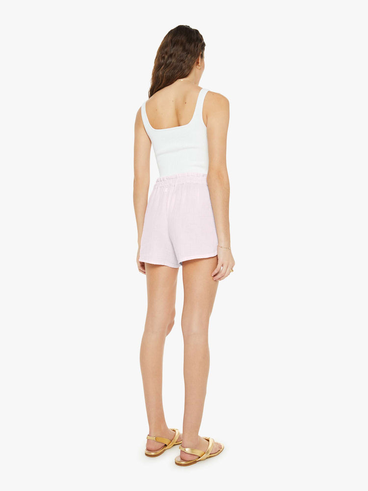 Back view of a woman in light pink shorts with a drawstring elastic waistband, curved hems and a loose, flowy fit.