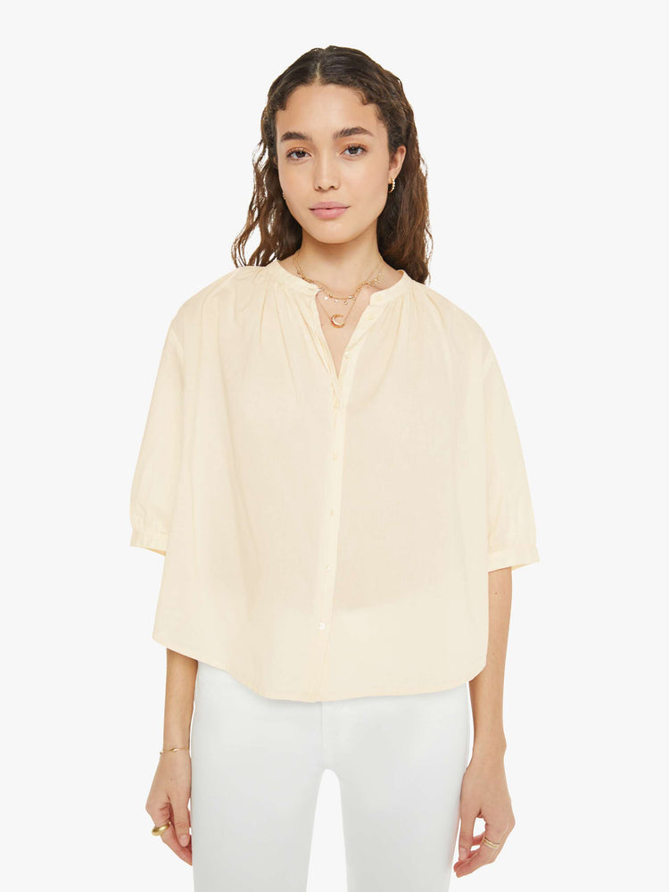 Front view of a woman in a creamy peach shirt that features a V-neck, elbow-length sleeves and ruffles throughout for a loose, flowy fit.