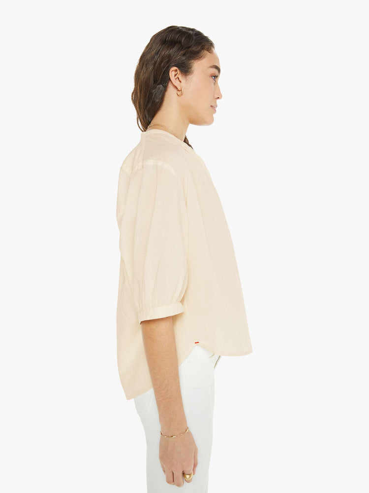 Side view of a woman in a creamy peach shirt that features a V-neck, elbow-length sleeves and ruffles throughout for a loose, flowy fit.