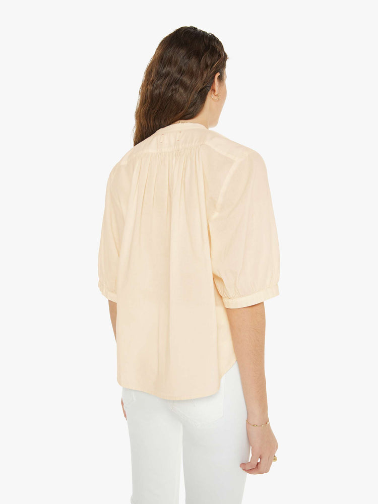 Back view of a woman in a creamy peach shirt that features a V-neck, elbow-length sleeves and ruffles throughout for a loose, flowy fit.