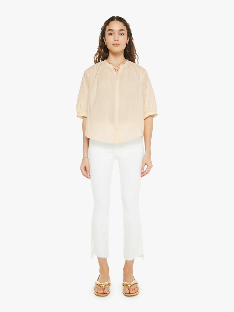 Full front view of a woman in a creamy peach shirt that features a V-neck, elbow-length sleeves and ruffles throughout for a loose, flowy fit.