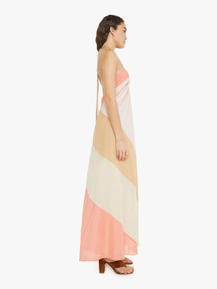 Side view of a woman in a blush-toned striped halter dress with  a calf-length hem and ruffles at the bodice for a loose flowy fit.