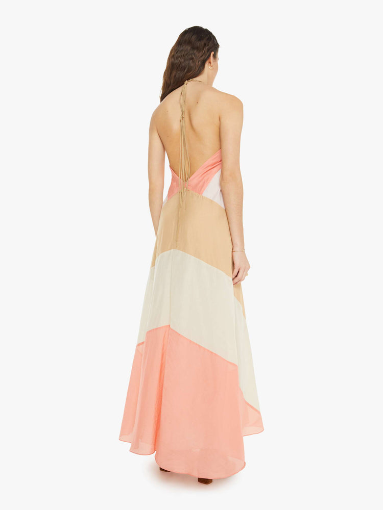 Back view of a woman in a blush-toned striped halter dress with  a calf-length hem and ruffles at the bodice for a loose flowy fit.