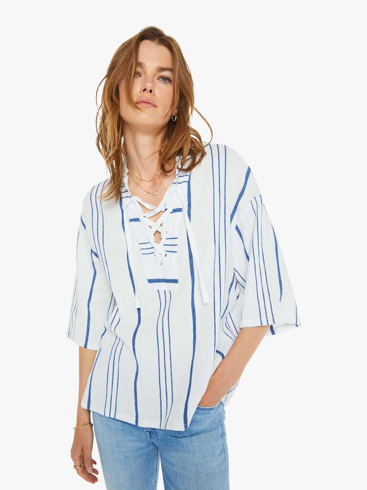 Front view of a woman in a white and blue striped blouse  designed with a V-neck that laces and ties, drop shoulders, elbow length sleeves and a loose, boxy fit. 