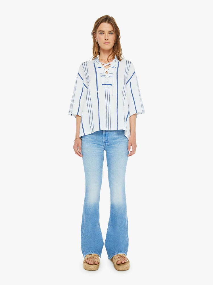 Full front view of a woman in a white and blue striped blouse  designed with a V-neck that laces and ties, drop shoulders, elbow length sleeves and a loose, boxy fit. 